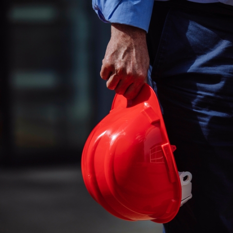 Male worker holding red hard hat at building site